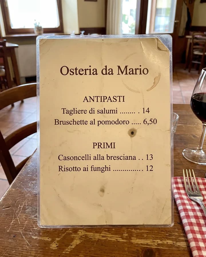 Foto del menu di carta di un'osteria, ingiallito e un po' macchiato, sul tavolo del locale